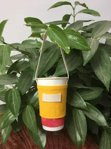 Detailaufnahme des gelben Leinenbecherhalters mit Trageriemen für Kaffee und Milchtee.