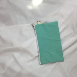 Nahaufnahme einer mintgrünen Canvas-Geldbörse mit weißem Reißverschluss und Metallring.