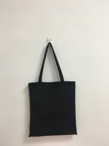Vista detallada de un bolso tote de lona negra simple colgado en la pared para uso diario.