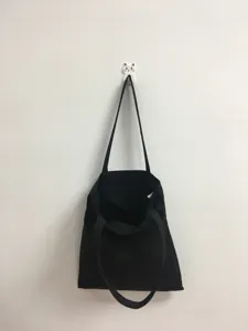 Vista detallada de un bolso shopper de lona negra lisa colgado en la pared, minimalista.