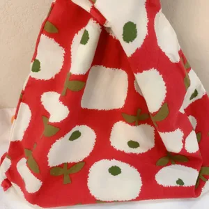 Close-up detail of Japanese style red cotton knot bag with cute white apple floral print pattern.