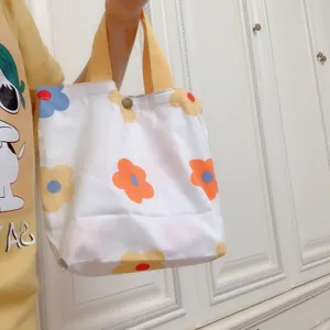 Lässige Segeltuchtasche mit buntem Blumenmuster und robusten gelben Griffen.