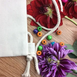 Detail view of blank white canvas drawstring bag decorated with colorful beads and fresh flowers.