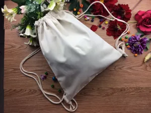 Detail shot of blank canvas drawstring backpack on wooden background with floral decor.