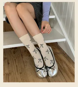 Primo piano di calzini beige a metà polpaccio con fiocchi neri e scarpe argento a punta divisa.