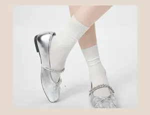 Detailopname van witte geribbelde dameskousen gecombineerd met stijlvolle zilveren platte schoenen.