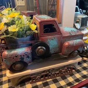 Vintage metal pickup truck decor with flower pot and rustic distressed tabletop finish.