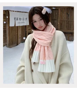 Close-up of stylish pink and white knitted winter scarf worn outdoors in snowy scene.