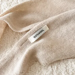 Primo piano dettagliato della sciarpa in lana beige lavorata a maglia con etichetta.