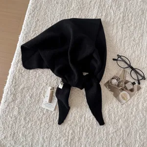 Dettaglio di sciarpa triangolare in maglia di lana nera con consistenza morbida e tessuto pregiato.