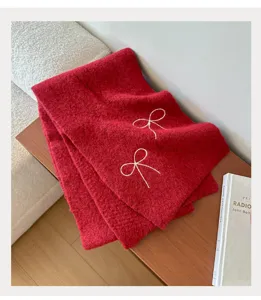 Cozy red knitted winter scarf close-up detail, featuring charming white embroidered bow accents.
