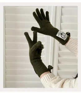 Detail shot of dark green knit split-finger gloves with ribbon bow and letter patch.