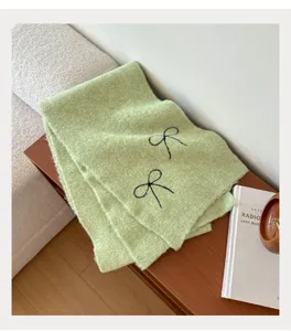 Detailed view of light green knitted scarf with black bow embroidery, cozy winter fashion.