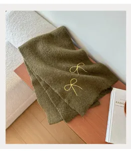 Detail view of olive green knitted winter scarf with cute yellow bow embroidery for women.