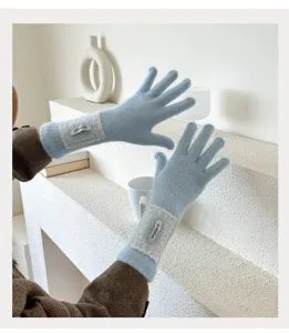 Nahaufnahme hellblauer Strickhandschuhe mit eleganter weißer Spitzenborte und Etikett.