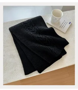 Detailansicht eines weichen schwarzen Strickschals mit Zopfmuster auf weißer Tischfläche.