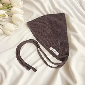 Close-up detail of dark brown knitted bonnet with string ties, soft wool texture close-up.