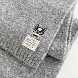 Close-up of grey knitted wool scarf featuring cute embroidered dog and brand label detail.