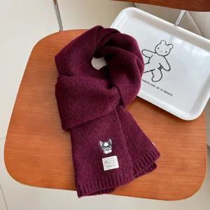Close up of cozy winter wool knit scarf featuring cute embroidered dog patch and label detail.