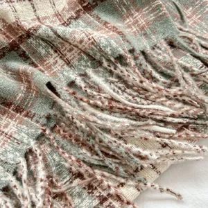 Close-up detail of green and brown plaid knitted scarf with soft decorative fringes.