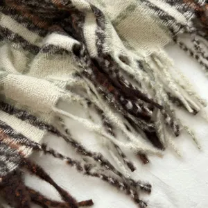 Close-up detail of cozy textured plaid winter scarf with soft fringes and warm tone pattern.