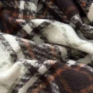 Close-up detail of cozy plaid scarf texture, soft boucle yarn fabric in brown and green tones.