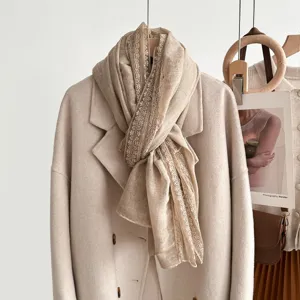 Detailed view of a women's beige lace trim scarf hanging gracefully on a coat rack.
