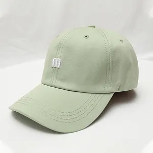 Close-up detail of sage green baseball cap featuring white 3d m embroidery and curved brim.