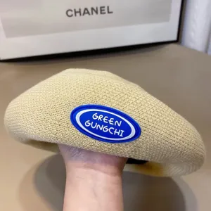 Knit beret hat detail view, beige woven retro style painter hat with rubber logo patch.