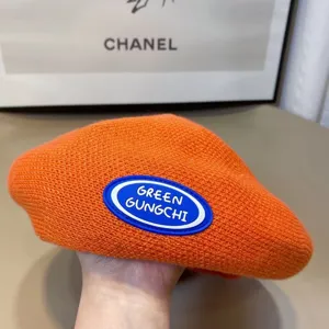 Close-up detail of orange knitted beret with blue white logo patch, vintage painter hat style.