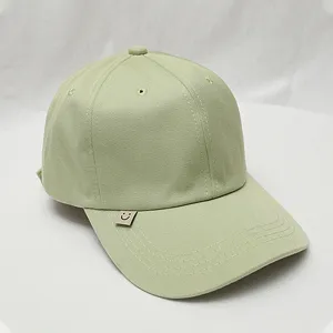 Light green baseball cap side detail showcasing cute metal smiley tag and clean stitching.