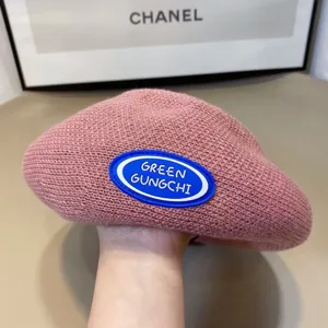 Knit beret close-up, pink colorway with blue oval logo patch, soft textured knit fabric.