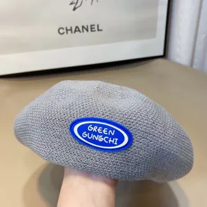 Detailed close-up of grey knitted beret featuring a blue rubber patch, soft texture style.