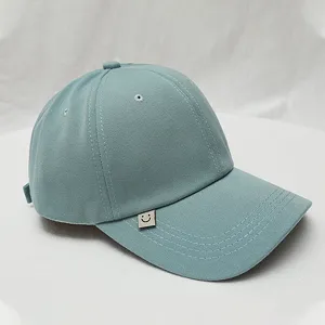 Close-up detail of the light blue-green baseball cap with a cute smiley face tag.