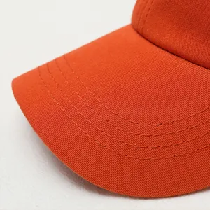 Close-up detail of orange baseball cap curved brim with precision parallel stitching texture.