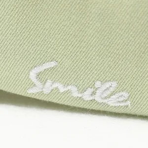 Green cotton baseball cap with white smile embroidery detail, casual curved brim sun hat.