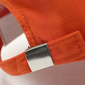 Detailed view of adjustable metal buckle and orange fabric strap on a casual baseball cap.