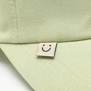 Close-up of light green baseball cap detail showing neat stitching and cute smiley label.