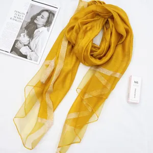 Detailed close-up of an elegant yellow silk-cotton scarf with shiny metallic stripe design.