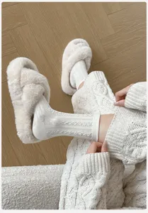Nahaufnahme gemütlicher weißer Zopfmuster Socken mit flauschigen Hausschuhen auf Holzfußboden.