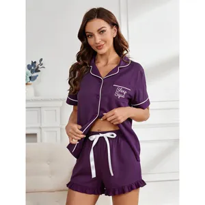 Detail shot of purple pajama set with white piping, chest pocket text, and matching shorts.