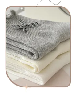 Detailansicht grauer und cremefarbener Socken mit Schleife, Rüschenrand und Feinstrick.