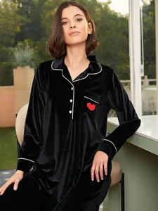Vista di dettaglio di un top pigiama in velluto nero con profilo bianco e cuore rosso.