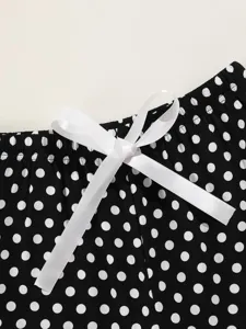 Close-up detail view of black and white polka dot lounge shorts featuring white ribbon bow.