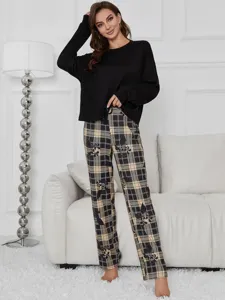 Cozy indoor lounge suit detail showing black long sleeve top and chic plaid plant print pants.