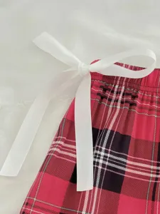 Close-up detail of women red black plaid lounge pants with white bow ribbon waist.