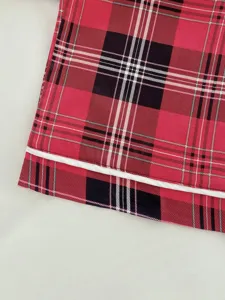 Close-up detail of red plaid rayon pajama pants with white piping. Soft fabric texture.