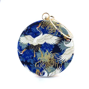 Close-up detail of the round clutch featuring intricate crane and floral patterns with gold hardware.