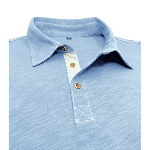 Close-up detail of light blue men's polo shirt collar, contrast stitching and wooden buttons.
