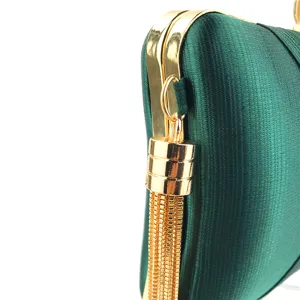 Green satin evening clutch bag detail, elegant gold metal frame with chic hanging tassel design.